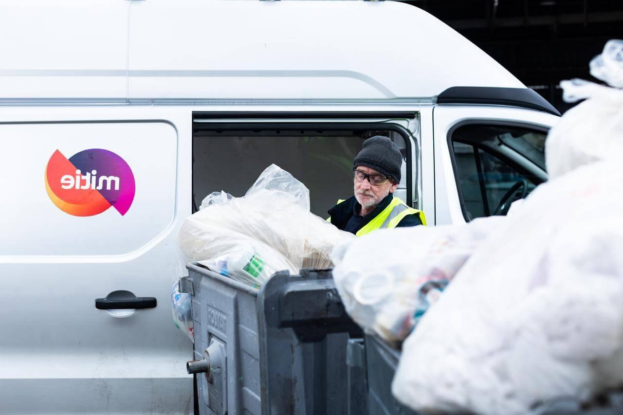 Mitie employee removing waste in plastic bags from roller bins, next to a van with the Mitie logo on the side
